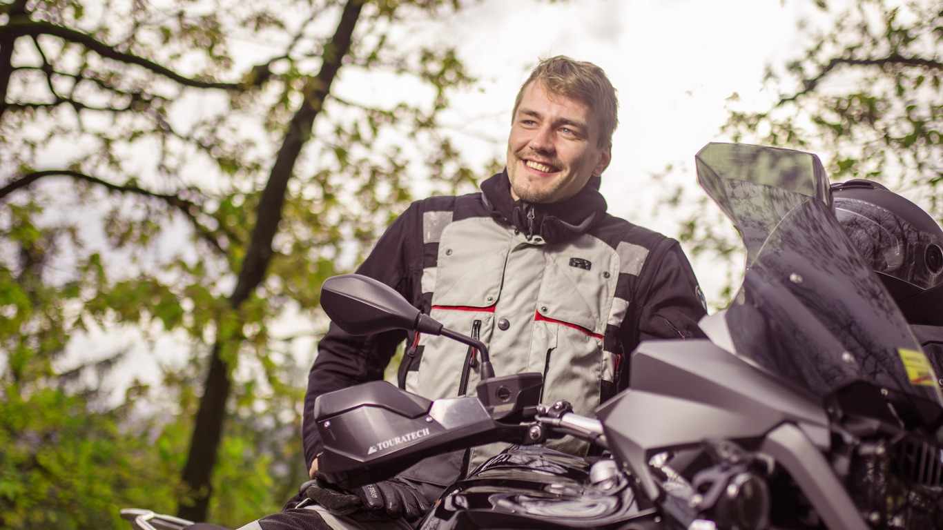 The dguard brand ambassador on a Honda Africa Twin stands in the woods and smiles. (Photo: digades GmbH))